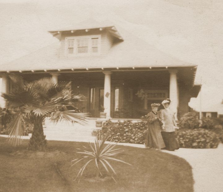 A house with a tree on it with 2 women walking in front